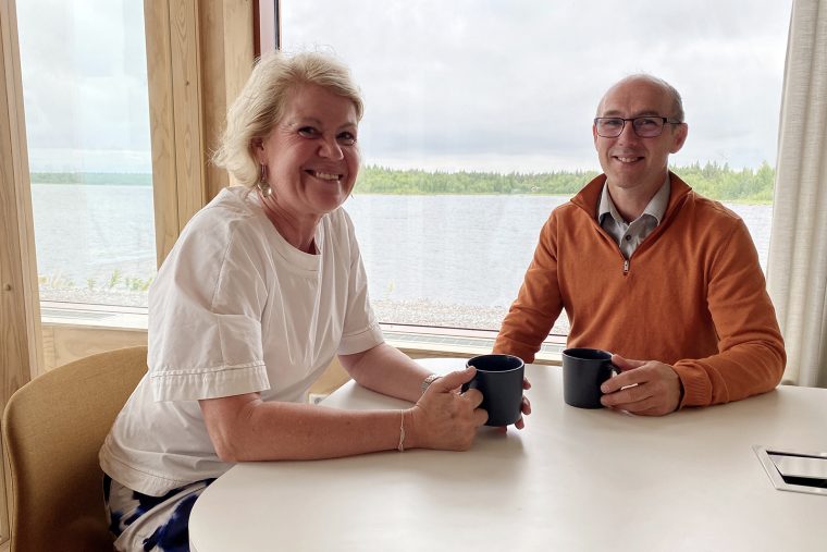 Bilden visar en kvinna och en man som sitter i ett konferensrum. I bakgrunden syns havet.